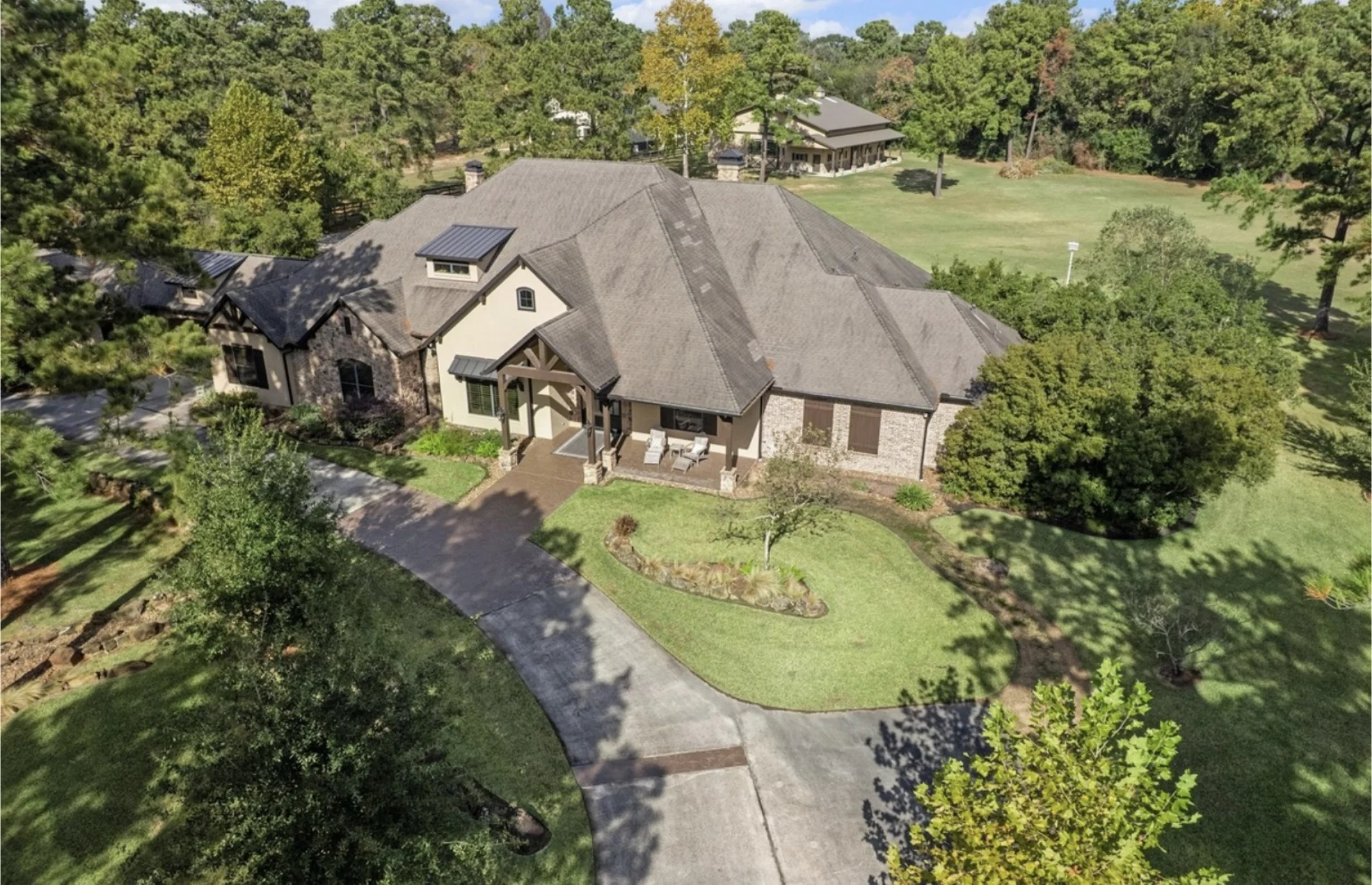 Aerial view of a large residential property with an expansive shingle roof and circular driveway